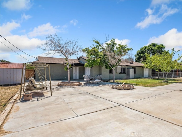 back of property featuring a patio area, fence, a shed, a fire pit, and stucco siding