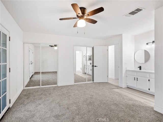 unfurnished bedroom with light carpet, a sink, a ceiling fan, baseboards, and visible vents