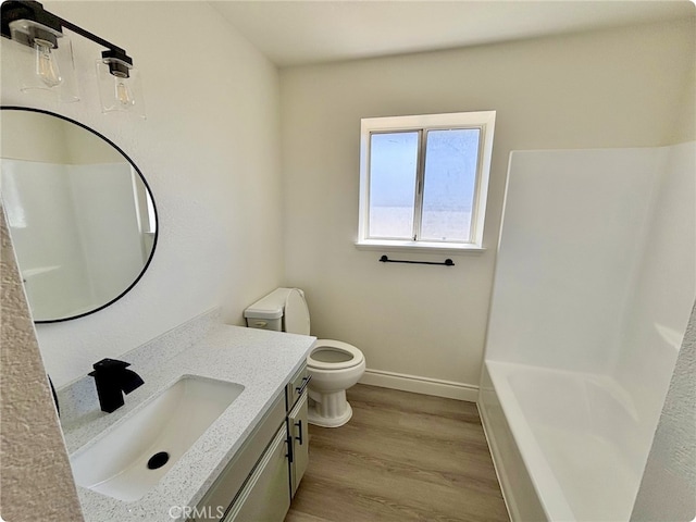 bathroom with a washtub, wood finished floors, baseboards, vanity, and toilet
