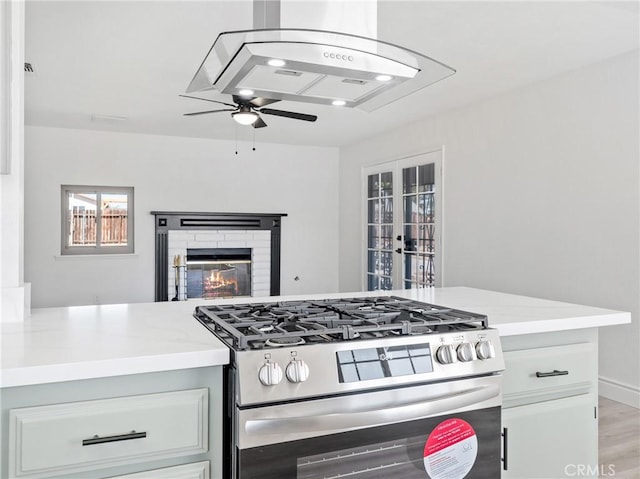 kitchen with stainless steel gas range, a fireplace, light countertops, french doors, and a ceiling fan