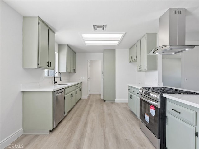 kitchen with appliances with stainless steel finishes, wall chimney exhaust hood, a sink, baseboards, and light wood-style flooring