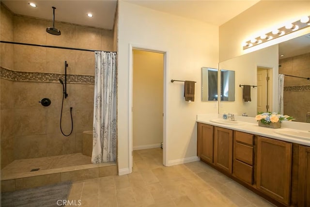 full bath featuring double vanity, tile patterned flooring, a sink, baseboards, and tiled shower
