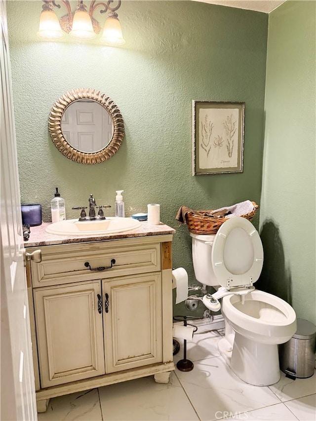 bathroom featuring vanity, marble finish floor, a textured wall, and toilet