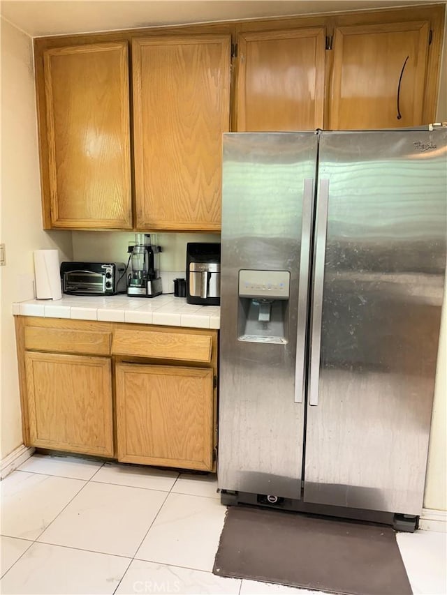 kitchen with stainless steel refrigerator with ice dispenser, tile counters, light tile patterned floors, and a toaster