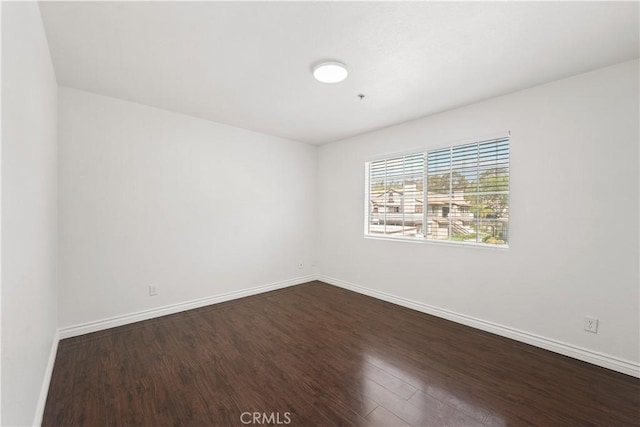 unfurnished room with baseboards and dark wood-style flooring