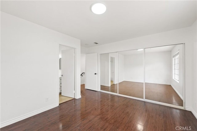unfurnished bedroom featuring baseboards, a closet, wood finished floors, and visible vents