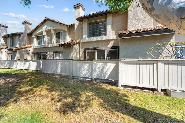 rear view of property featuring a chimney, a tile roof, a lawn, fence, and stucco siding
