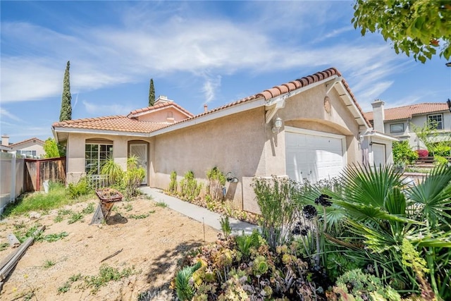 mediterranean / spanish home with a tiled roof, an attached garage, fence, and stucco siding