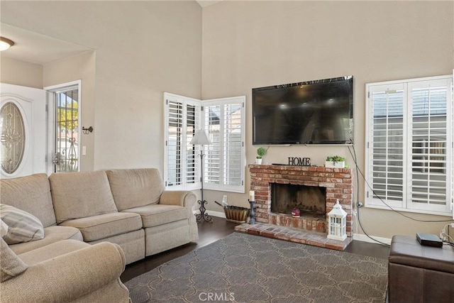 living area featuring a brick fireplace, baseboards, wood finished floors, and a high ceiling