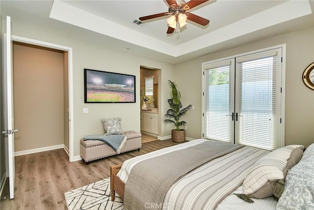 bedroom featuring access to outside, a raised ceiling, french doors, light wood-style flooring, and baseboards