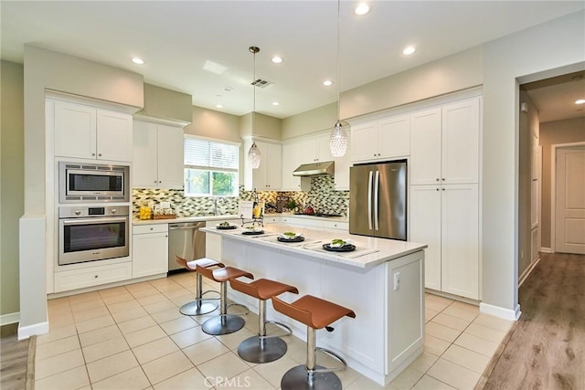 kitchen featuring tasteful backsplash, under cabinet range hood, white cabinets, and stainless steel appliances