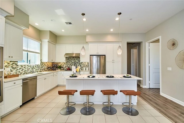 kitchen with visible vents, under cabinet range hood, a sink, appliances with stainless steel finishes, and backsplash