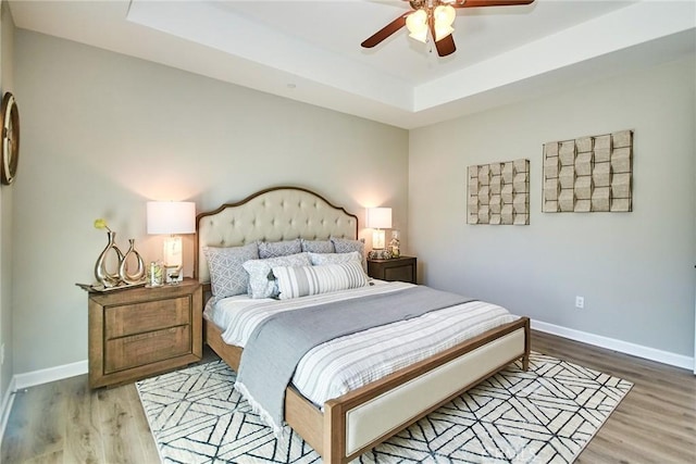 bedroom featuring baseboards, a ceiling fan, light wood-style flooring, and a tray ceiling