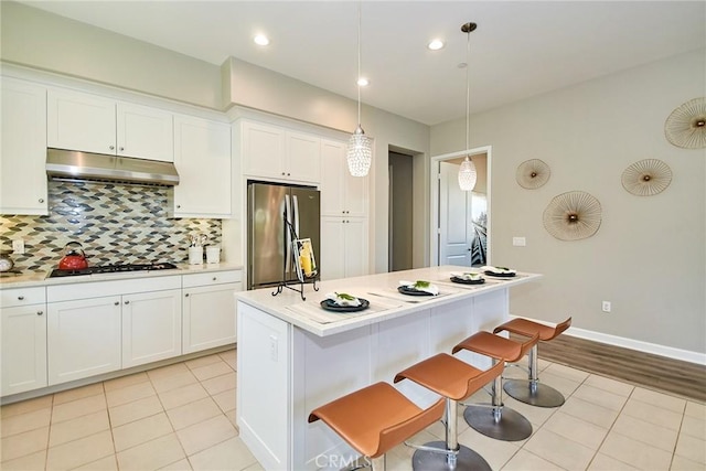 kitchen with backsplash, stainless steel refrigerator, light countertops, under cabinet range hood, and white cabinetry