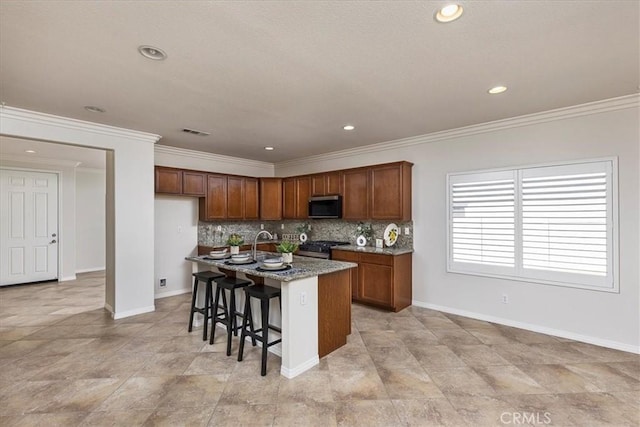 kitchen with visible vents, baseboards, stainless steel microwave, and a kitchen island with sink