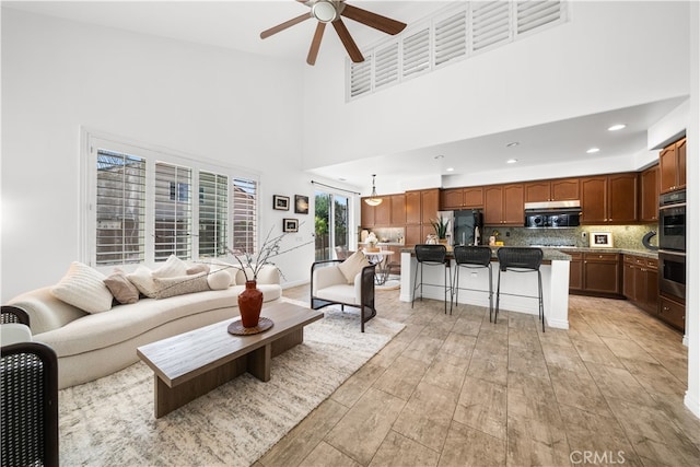 living room with ceiling fan, recessed lighting, light wood-style flooring, and a high ceiling
