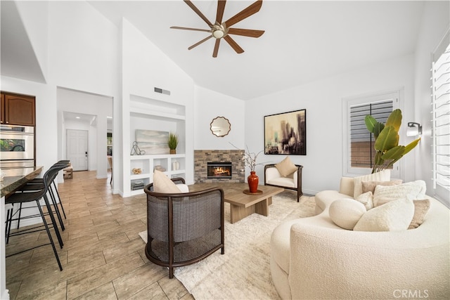 living room featuring a ceiling fan, visible vents, built in features, a fireplace, and high vaulted ceiling