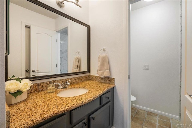 bathroom featuring toilet, baseboards, stone finish floor, and vanity
