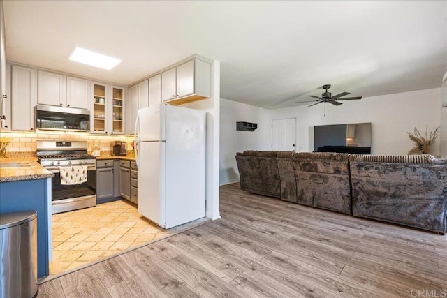 kitchen featuring glass insert cabinets, open floor plan, tasteful backsplash, a ceiling fan, and appliances with stainless steel finishes