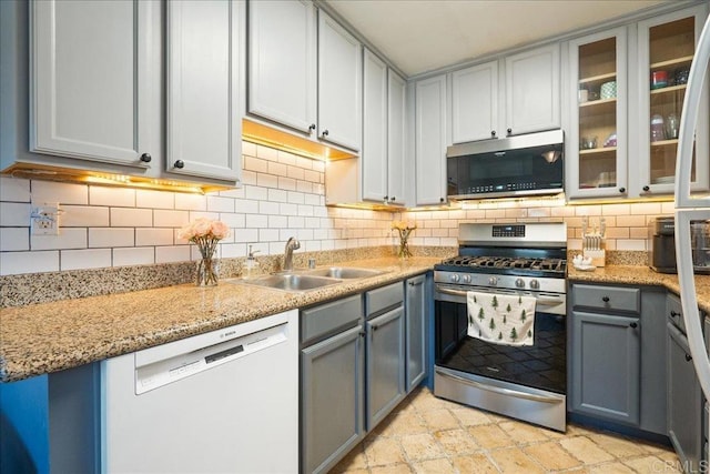 kitchen with a sink, gray cabinets, appliances with stainless steel finishes, and tasteful backsplash
