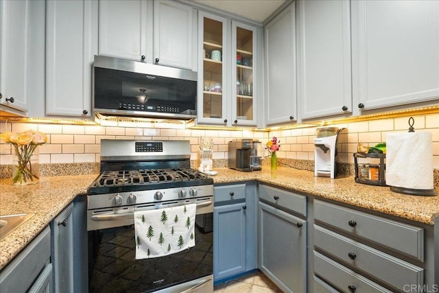 kitchen with backsplash, appliances with stainless steel finishes, glass insert cabinets, and gray cabinets