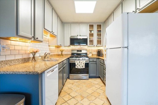 kitchen with light stone countertops, gray cabinets, tasteful backsplash, a sink, and stainless steel appliances