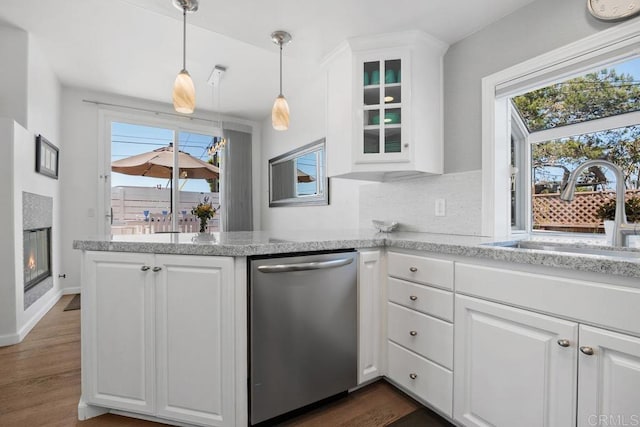 kitchen with a sink, white cabinetry, a peninsula, stainless steel dishwasher, and glass insert cabinets