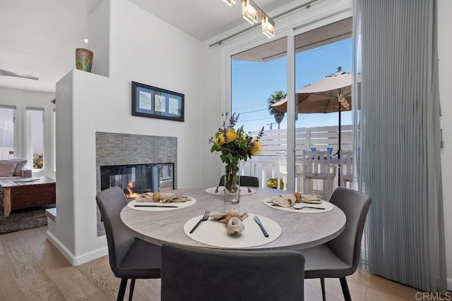 dining space with a multi sided fireplace, baseboards, a healthy amount of sunlight, and light wood-type flooring