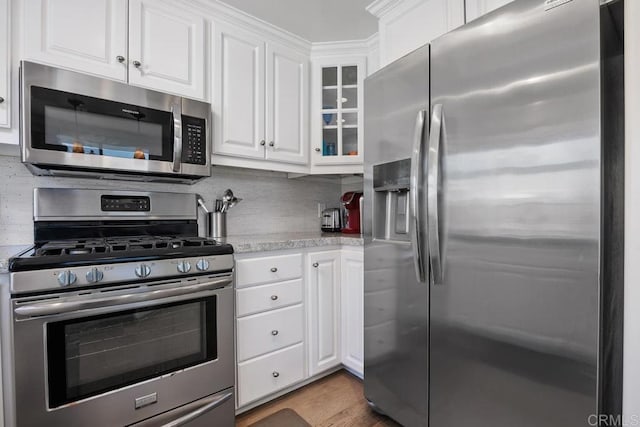 kitchen featuring glass insert cabinets, light countertops, white cabinets, tasteful backsplash, and appliances with stainless steel finishes
