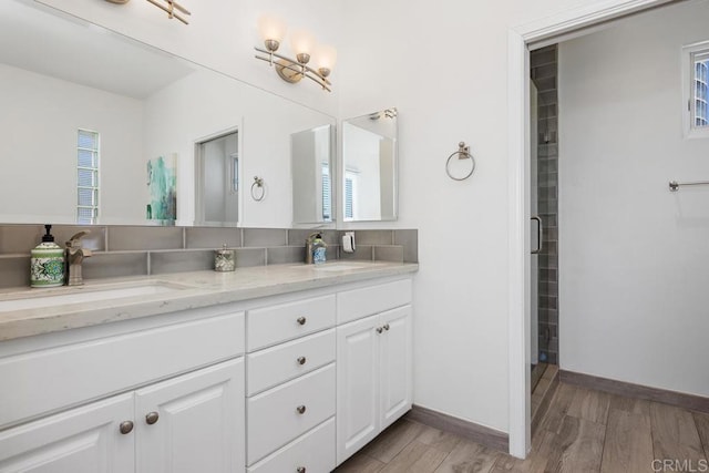 full bathroom featuring a sink, baseboards, double vanity, and wood finished floors