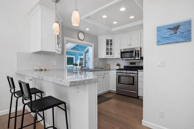 kitchen featuring ornamental molding, glass insert cabinets, a breakfast bar area, white cabinets, and appliances with stainless steel finishes