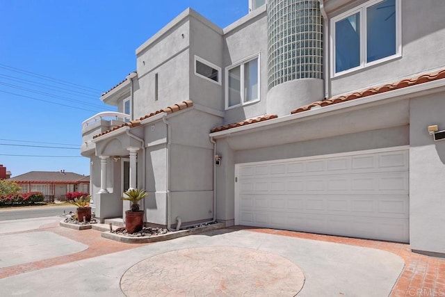 view of front facade featuring curved driveway, an attached garage, a tile roof, and stucco siding