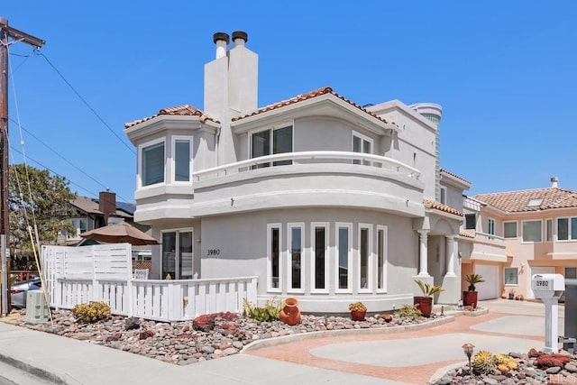 view of front of home with a tiled roof, stucco siding, a balcony, and a chimney