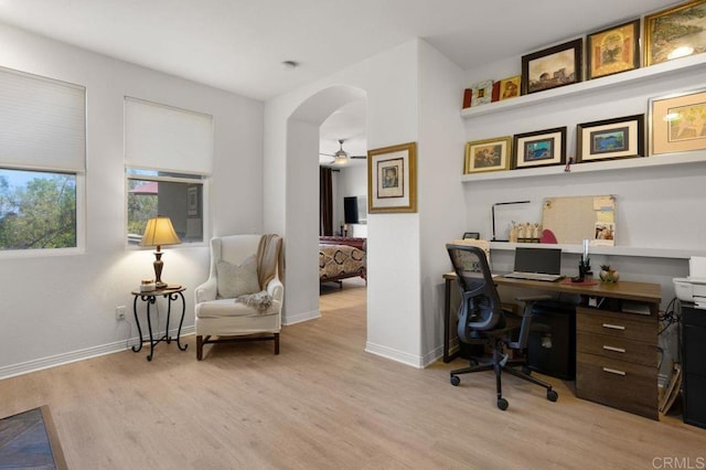 office space with arched walkways, ceiling fan, baseboards, and light wood finished floors