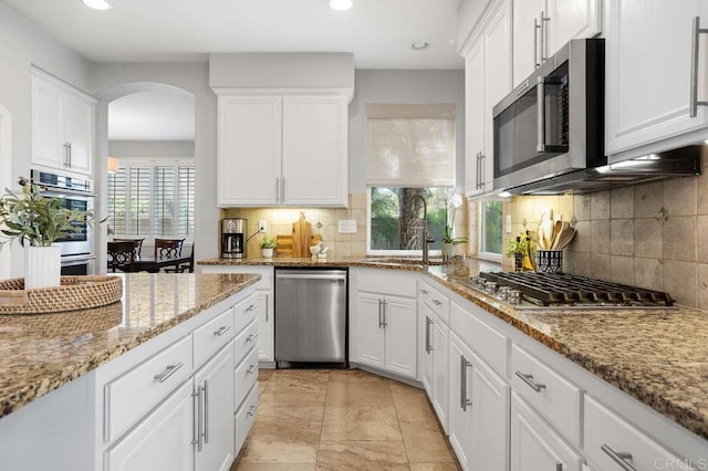 kitchen with decorative backsplash, appliances with stainless steel finishes, white cabinets, and a wealth of natural light