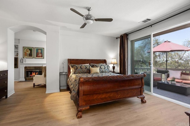 bedroom with visible vents, wood finished floors, access to outside, a tiled fireplace, and arched walkways