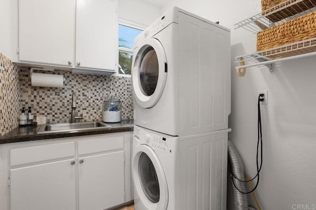 laundry room featuring cabinet space, stacked washing maching and dryer, and a sink