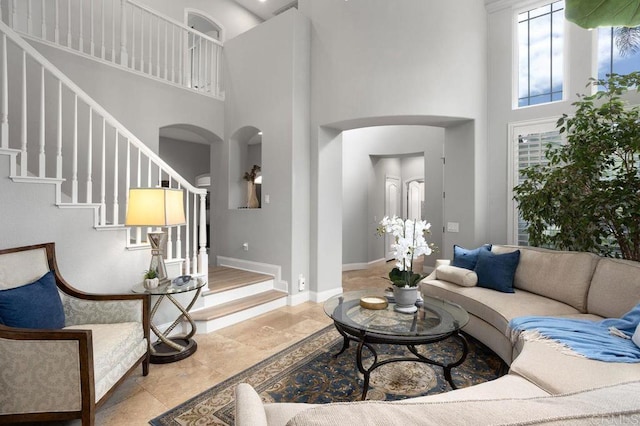 living room featuring stairs, arched walkways, a high ceiling, and baseboards