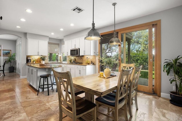 dining room featuring visible vents, stone tile floors, baseboards, recessed lighting, and arched walkways