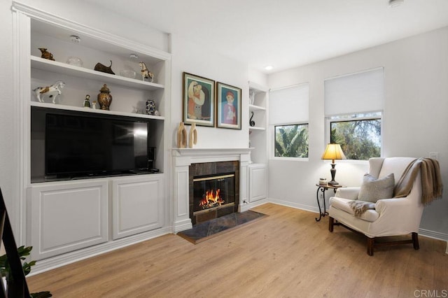 sitting room with built in features, baseboards, a fireplace, and light wood finished floors