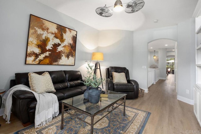 living room featuring arched walkways, baseboards, ceiling fan, and light wood finished floors