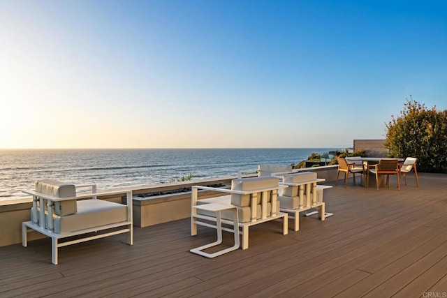 deck at dusk with a water view and outdoor dining area