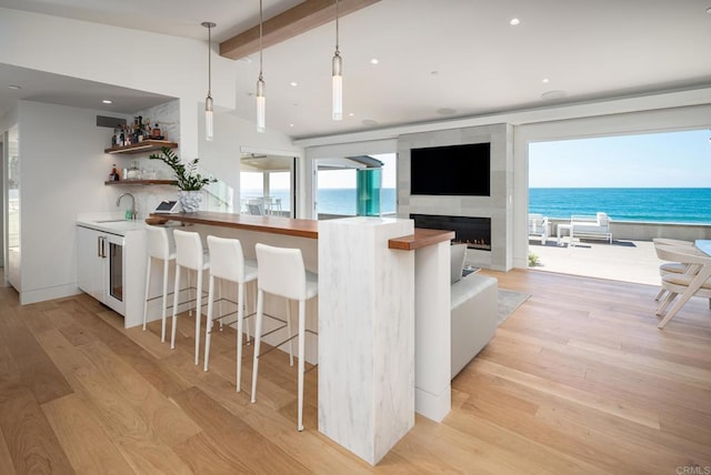 kitchen with a breakfast bar area, pendant lighting, a sink, light wood finished floors, and vaulted ceiling with beams