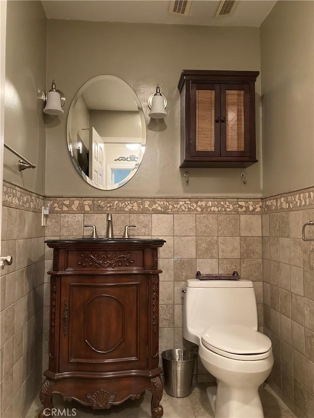 half bath featuring vanity, toilet, tile walls, and a wainscoted wall