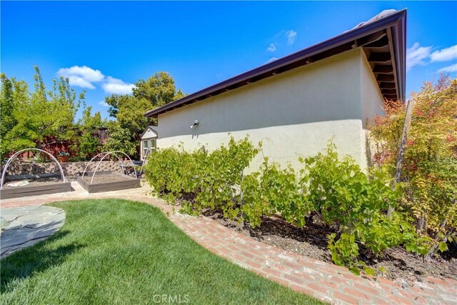 view of property exterior with stucco siding, a yard, and a vegetable garden