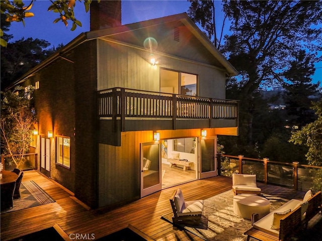 back of house at night with an outdoor living space, a balcony, a chimney, and a deck