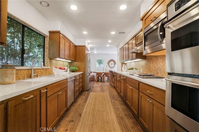 kitchen featuring brown cabinets, a sink, light countertops, stainless steel appliances, and light wood-style flooring