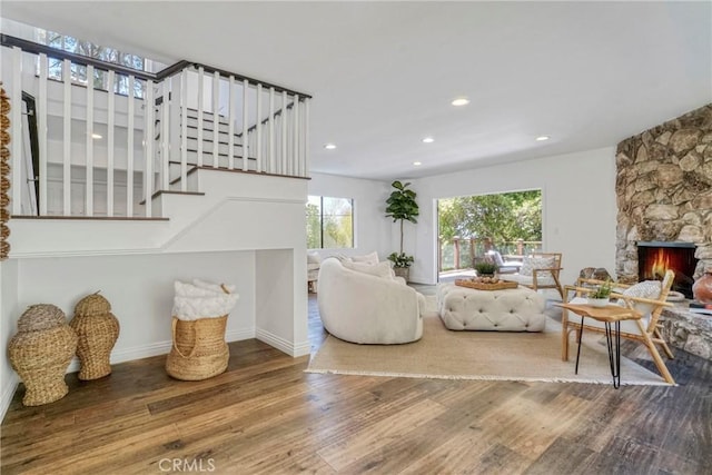 living room with stairway, a stone fireplace, recessed lighting, and wood finished floors