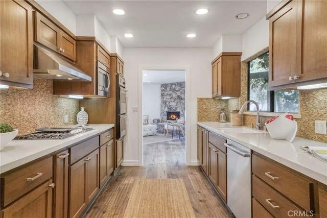 kitchen featuring a sink, light countertops, stainless steel appliances, wood finished floors, and under cabinet range hood