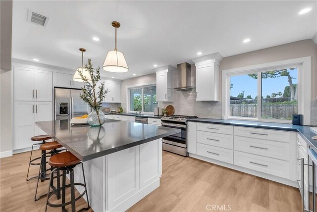 kitchen featuring wall chimney range hood, appliances with stainless steel finishes, dark countertops, and visible vents